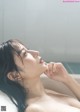 A woman in a bathtub with water droplets on her face.