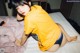 A woman in a yellow shirt is sitting on a bed.